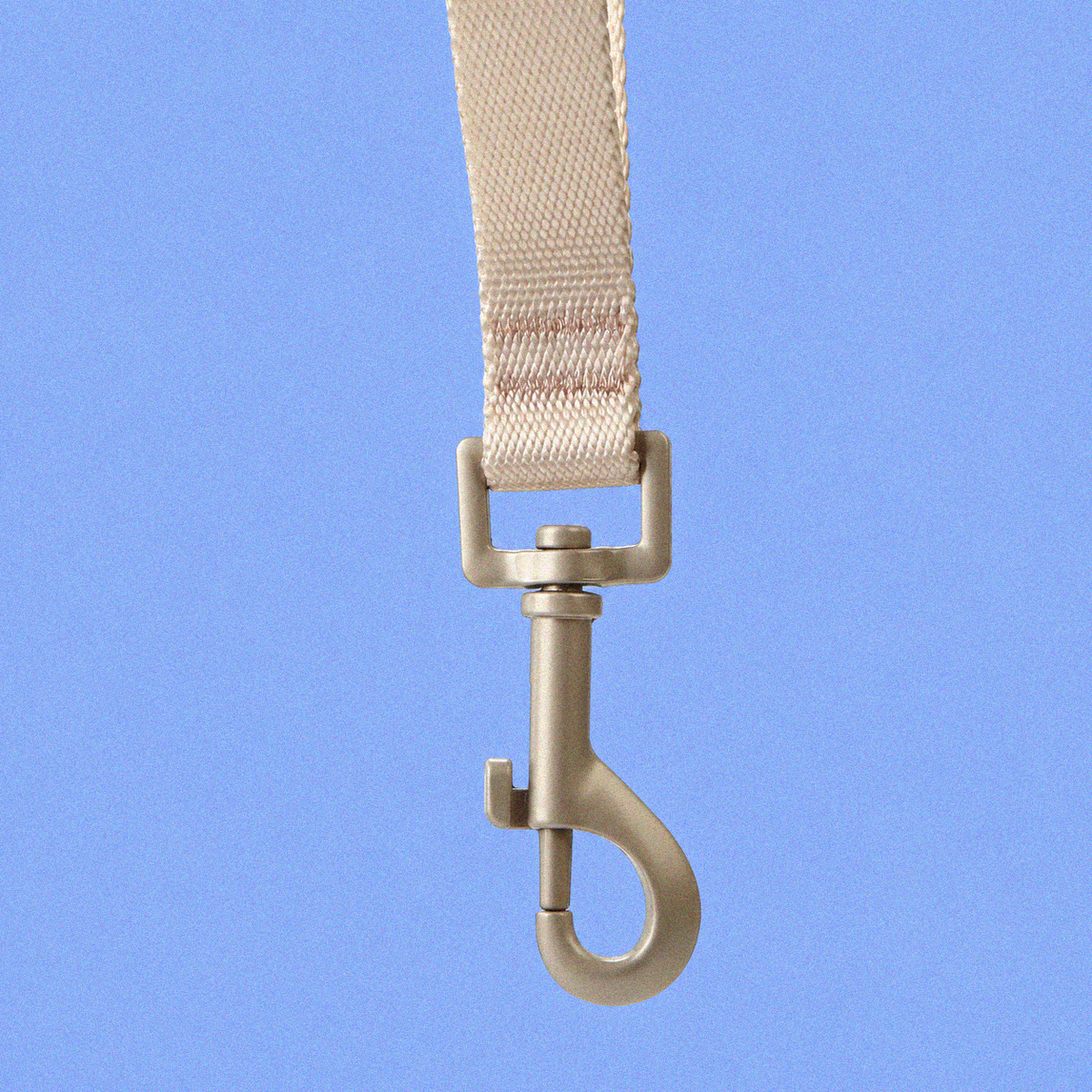 A close-up of a beige woven strap with a silver metal swivel snap hook, shown against a solid blue background.
