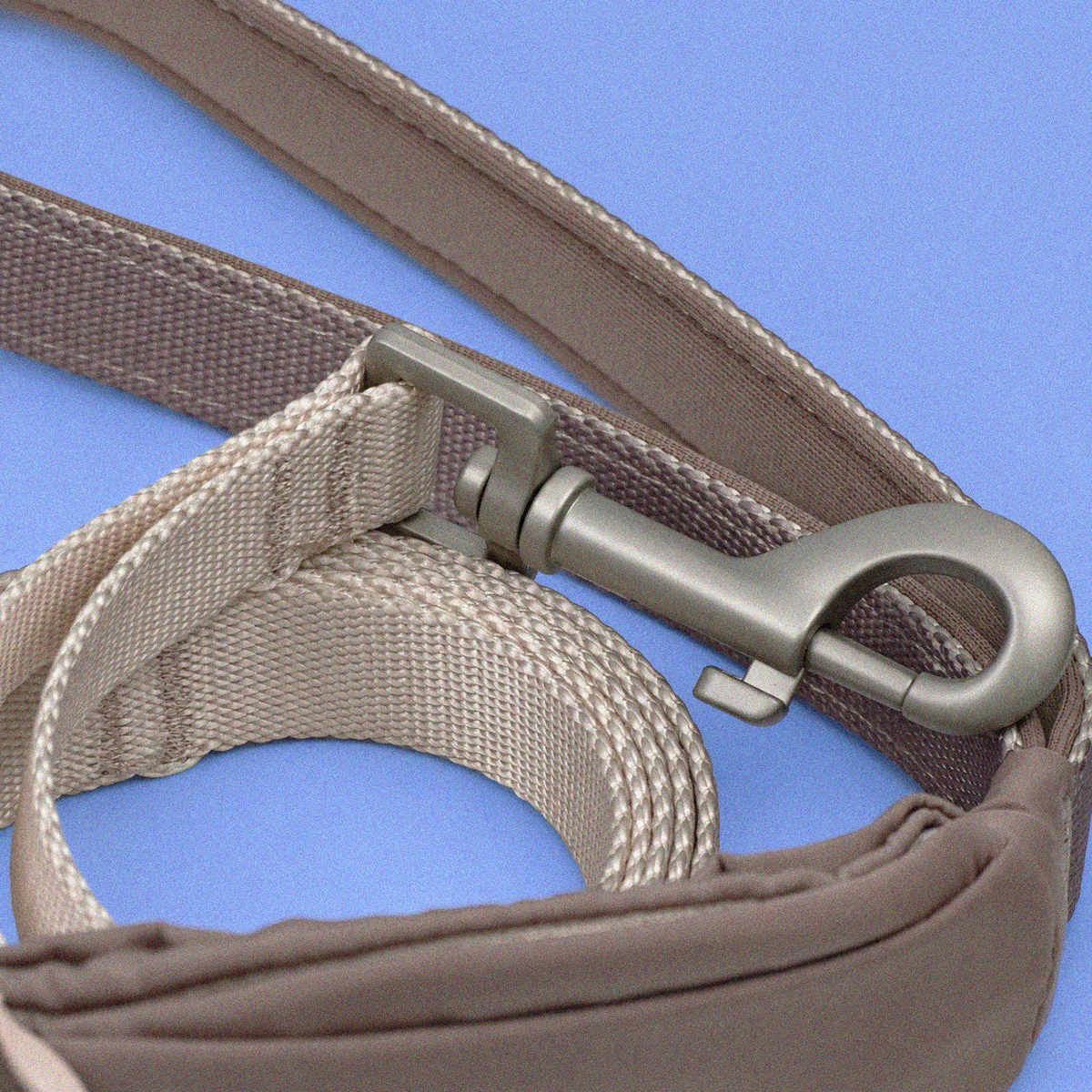 Close-up of a taupe fabric strap with a silver metal clip attached, laid against a solid blue background.